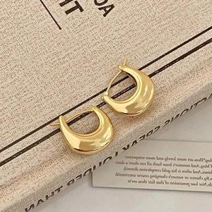 Macro detail of polished gold-plated thick hoop earrings on a textured fabric background