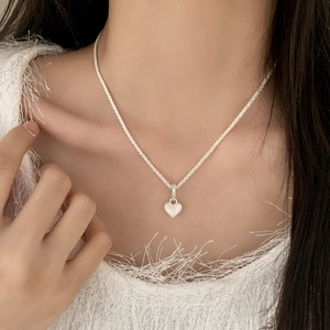 Collier élégant avec pendentif cœur, pierre blanche et bordure perlée en argent sur modèle