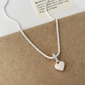 Gros plan du collier cœur en argent avec incrustation de nacre sur support papier