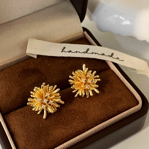 Macro detail of gold radial firework studs with white zircons on a velvet box