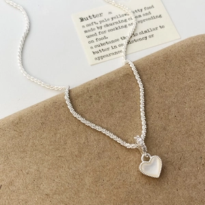 Détail du collier cœur en argent avec nacre blanche et bordure perlée élégante