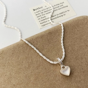 Détail du collier argenté avec pendentif cœur et incrustation nacrée sur carte décor