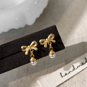 Detail view of gold bow-knot pearl earrings on a display stand with a handmade aesthetic