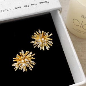 Macro shot of gold starburst earrings with white rhinestones and pearls on black velvet