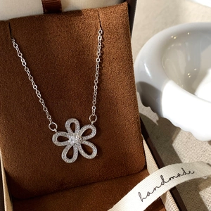 Macro shot of silver flower pendant with zircon inlay on brown velvet jewelry box
