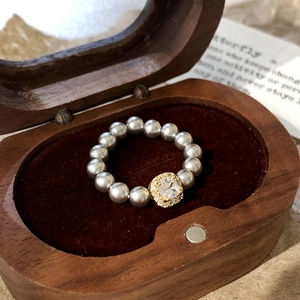 Macro shot of grey pearls and square-cut zircon stone on golden ring in a wooden box