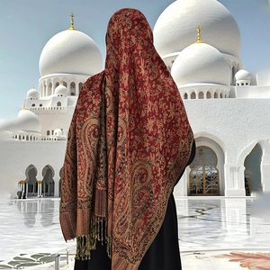 Detailed view of luxury red and gold paisley shawl with fringes against a white mosque background