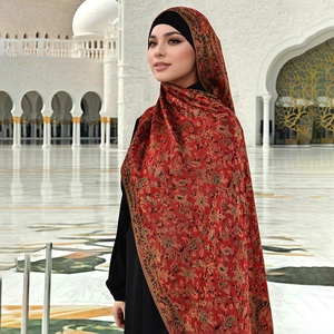 Detail of red ethnic shawl with gold paisley patterns and fringes against white arches