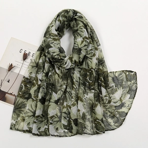 Flat lay of a lightweight floral printed long scarf with green leaf patterns and accessories