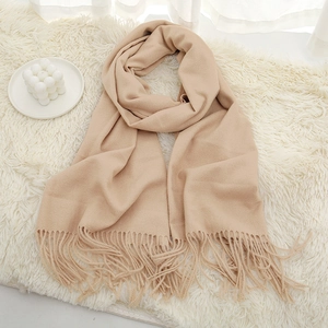 Detail view of a thick beige tassel scarf with soft cashmere-like texture on a white rug