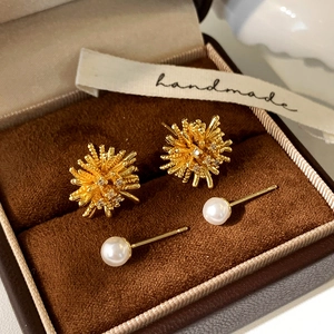 Macro shot of gold firework zircon studs and elegant white pearl earrings on brown velvet