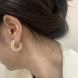 Boucles d'oreilles créoles dorées en C avec perles blanches portées de profil par un mannequin