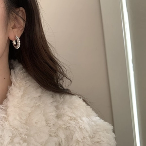 Détail de créoles argentées avec petites perles blanches portées par un mannequin élégant