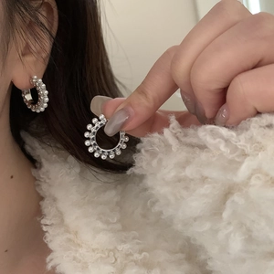 Détail de créoles argentées avec perles blanches incrustées sur fond blanc doux