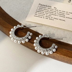 Gros plan de boucles d'oreilles argentées en C avec perles blanches sur fond en bois
