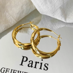 Macro shot of gold twist hoop earrings with mirror reflection on white fabric background