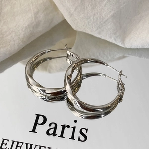 Detail of twisted silver hoop earrings with polished finish on a clean reflective surface
