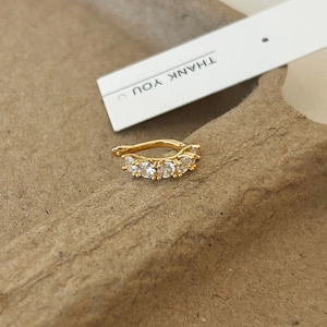 Detailed close-up of golden bow-shaped ear cuff with zircon stones on a card
