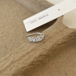 Detailed view of silver bow ear cuff with five inlaid cubic zirconia stones on textured card