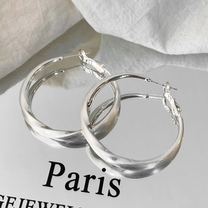 Detailed view of silver twisted hoop earrings with brushed metal finish on linen