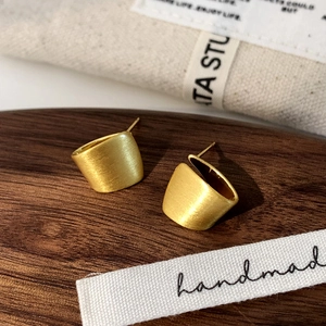 Nahaufnahme der matten goldenen geometrischen Ohrstecker mit gebürsteter Textur