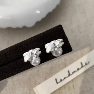 Detail of silver bow earrings with round white pearls on a textured display