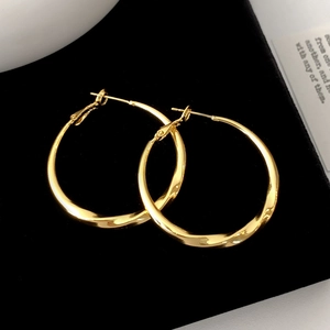 Detailed view of large golden twisted hoop earrings on black velvet background