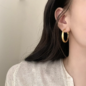 Minimalist golden geometric hoop earrings with brushed metal finish shown on a model
