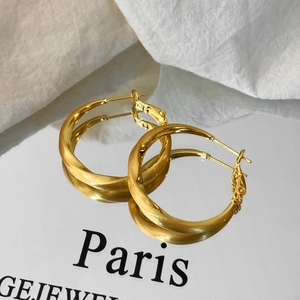 Detailed close-up of large twisted gold earrings with a textured brushed finish
