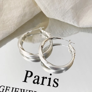 Close-up of silver irregular twisted hoop earrings with brushed metallic finish