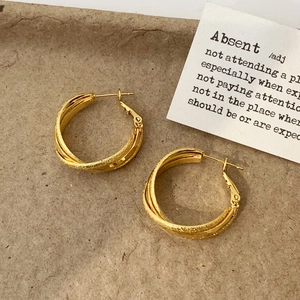 Macro detail of gold triple-intertwined textured hoop earrings on artful paper background
