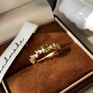Detailed close-up of handmade gold ring with square green gemstone and white zircons