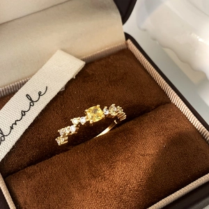 Detail of gold ring with square yellow gemstone and side diamonds in a brown velvet box