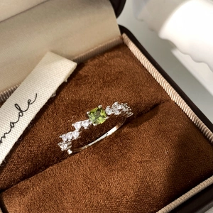 Macro shot of a thin gold ring with square green gemstone and diamonds in a jewelry box