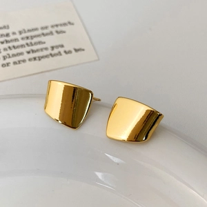 Polished gold geometric square stud earrings with mirror finish on a decorative tray