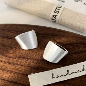 Macro shot of silver brushed metal geometric stud earrings on a walnut wood tray