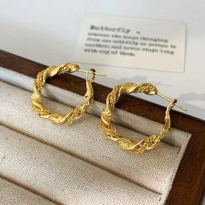 Detailed shot of golden twisted rope hoop earrings in a beige velvet jewelry box