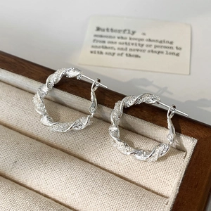 Detailed view of silver twisted hoop earrings with textured finish in a wooden jewelry box