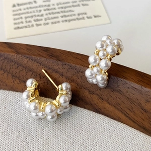 Close-up of elegant gold C-shaped hoop earrings with cluster white pearls on wood and cloth
