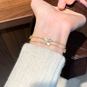 Dual-layer gold bracelet with zircon clover pendant on a white sweater background