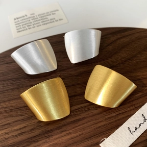 Minimalist brushed metal wide arch earrings in matte gold and silver on wooden tray