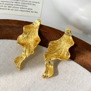 Macro detail of gold-plated earrings with irregular liquid metal texture on rustic background