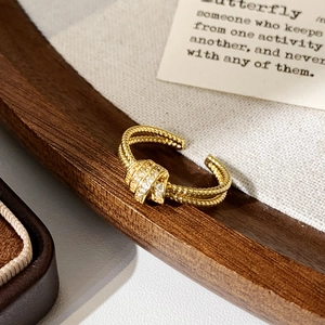 Close-up of golden double-layer knot ring with micro-set zircons on a rustic backdrop