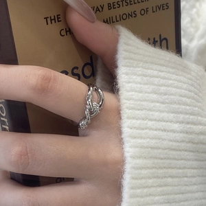 Minimalist silver knot ring on index finger with elegant casual knitwear background