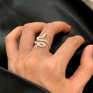Silver snake wrap ring with green gemstone eyes on a textured black leather background