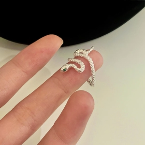 Detail shot of silver snake ring featuring green crystal eyes and textured scales