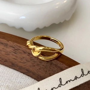 Detail view of a polished gold knotted ring displayed on a minimal textured background