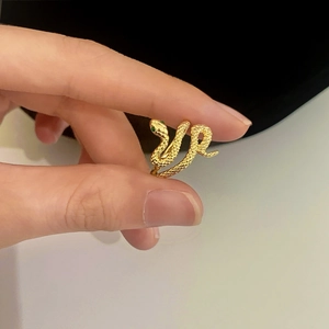 Detail of golden snake ring featuring green gemstone eyes and textured scale engraving
