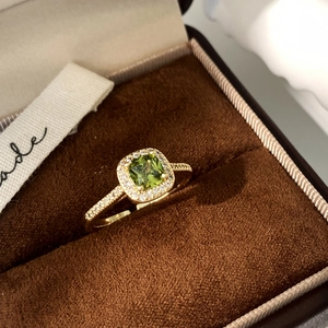 Macro detail of adjustable gold ring featuring a green square-cut stone and pavé accents