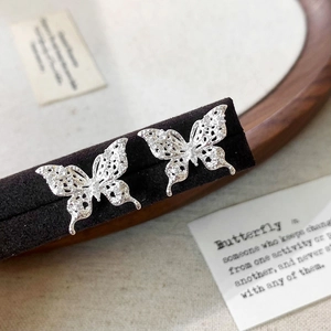 Detail of silver hollow butterfly stud earrings featuring a shimmering lace pattern
